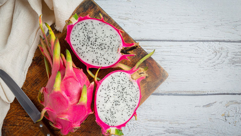 Dragon fruit cut in half, displaying its contrasting black seeds and white pulp against the pink rind.