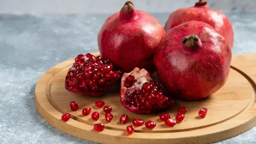 Ripe pomegranates with large, juicy seeds on a wooden board, a vivid example of fruits with big seeds.