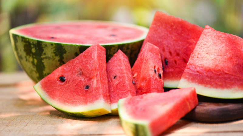 Juicy watermelon slices with black seeds on a wooden surface, epitomizing summer fruits.