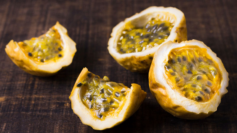 Granadilla fruits cut open to reveal black seeds encased in translucent pulp on a dark surface.