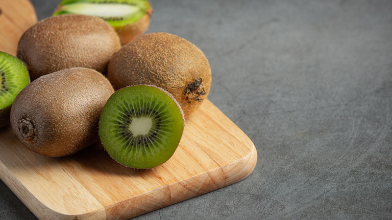 Kiwi fruits halved on a cutting board, revealing vibrant green flesh and tiny seeds.