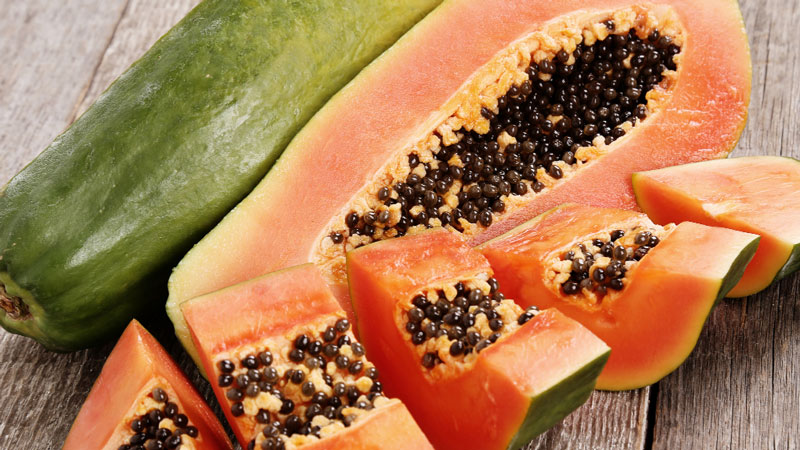 Ripe papaya with black seeds cut into slices on a rustic wooden table.
