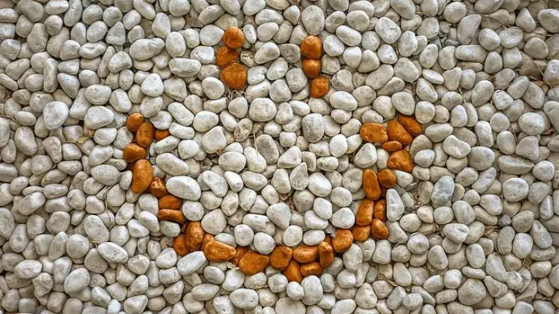 White gravel background creatively arranged with orange stones to form a smiling face, showcasing one of the kinds of gravel used in patio design.
