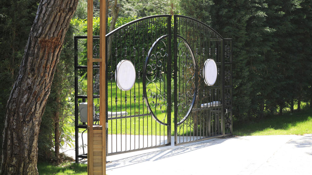 Elegant wrought iron gate with decorative scrolls and two oval plaques, poised to prevent gate slamming.