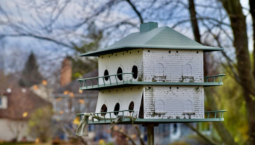 Multi-story birdhouse, weathered white paint, green roof, tranquil garden.