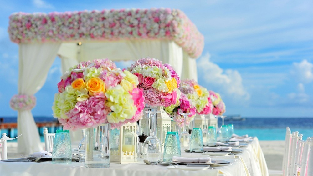 Beachfront wedding setup with floral centerpieces, white canopy, ocean view.