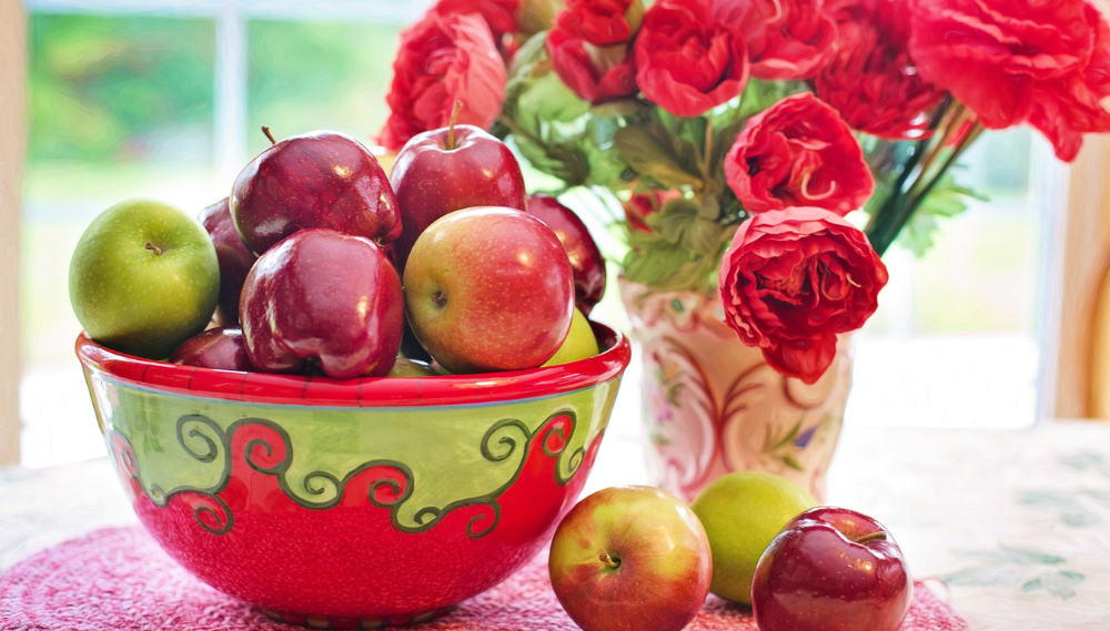 Wedding centerpiece: apples in bowl with red rose bouquet backdrop.