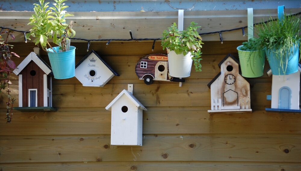 Charming birdhouses on wooden fence with potted plants, rustic display.