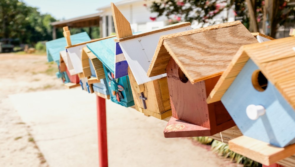 Colorful wooden birdhouses on red post along sunny outdoor pathway.