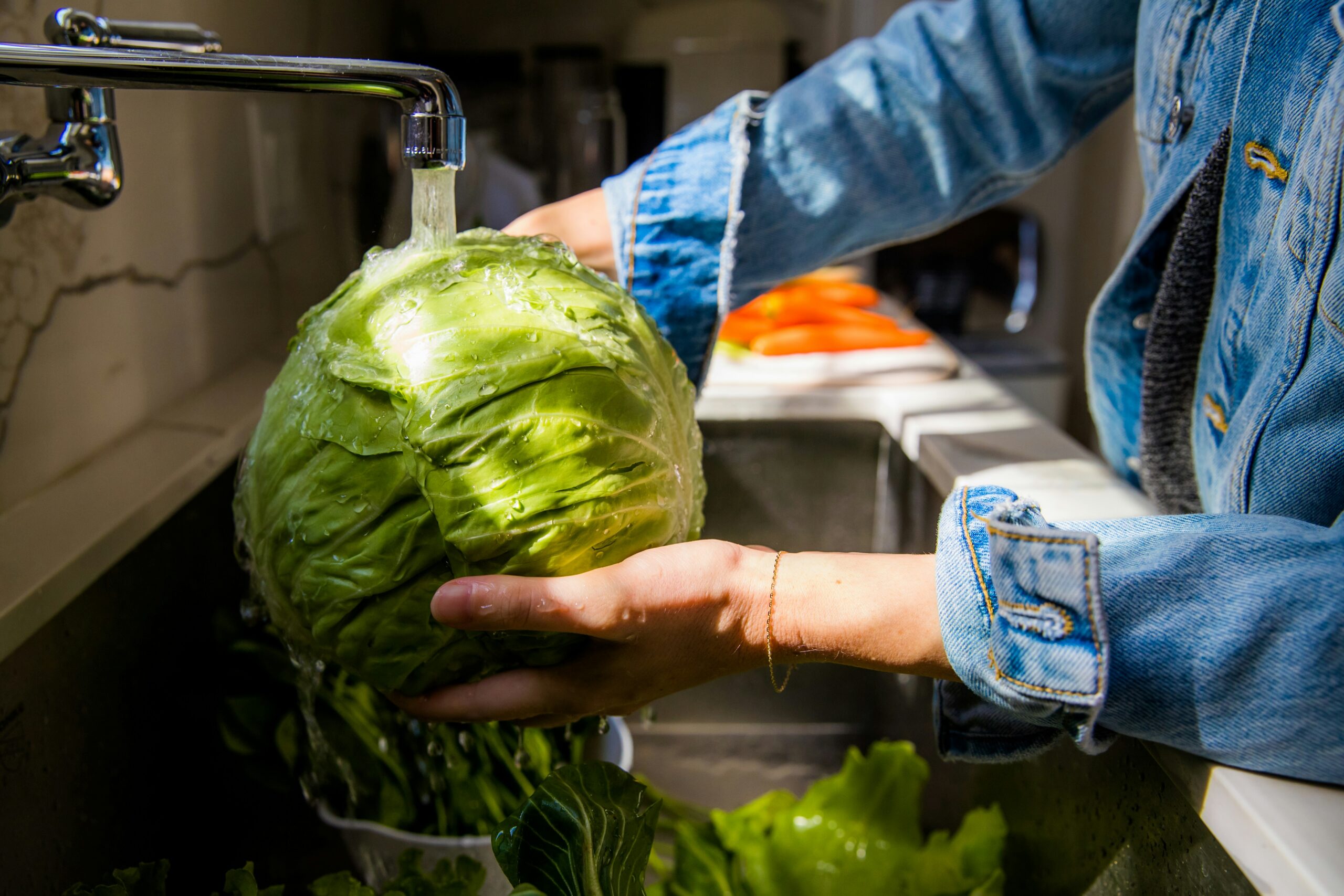 Hand rinsing a head of cabbage under a faucet.